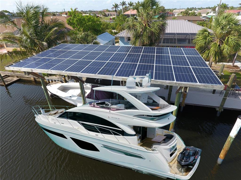 A large yacht and a smaller boat are docked under a solar panel roof structure — 107 SINCLAIR STREET SE, PORT CHARLOTTE, FL