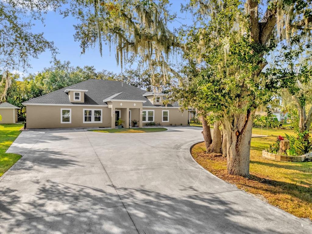 A single-story house with a large concrete driveway and mature trees in the front yard — 705 LENOX PLACE, KISSIMMEE, FL