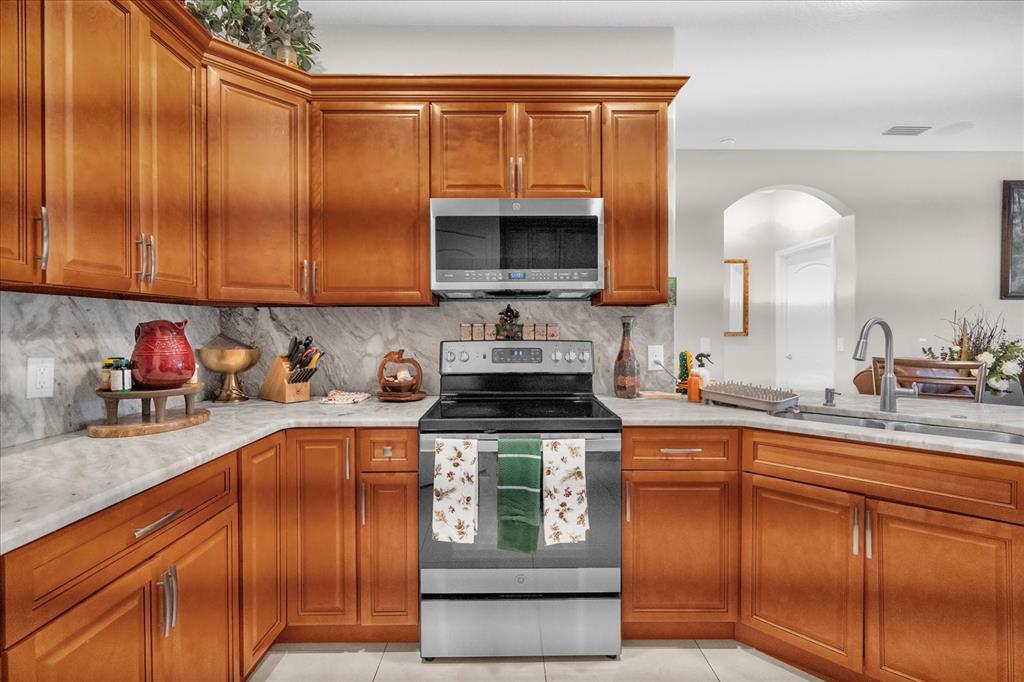 A kitchen features wood cabinets, stainless steel appliances, and a marble-patterned countertop and backsplash — 705 LENOX PLACE, KISSIMMEE, FL