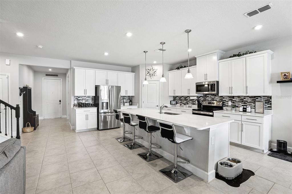 A modern kitchen features white cabinetry, stainless steel appliances, a quartz island, and tile flooring — 4000 CLIPSTONE PLACE, SANFORD, FL