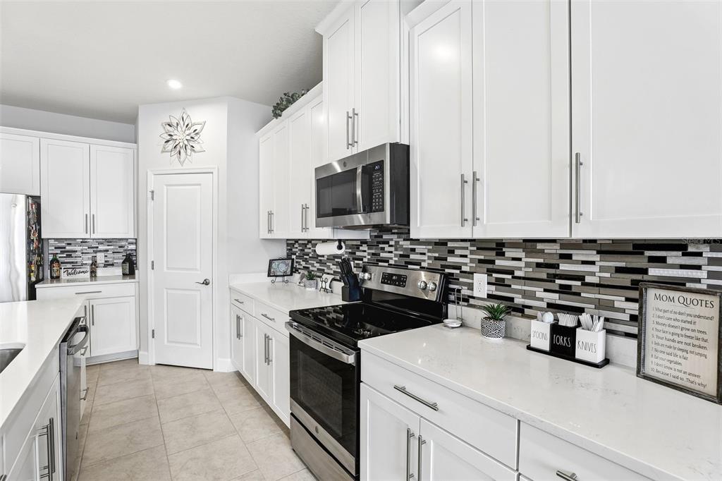 A kitchen features white cabinets, stainless steel appliances, quartz countertops, and a mosaic tile backsplash — 4000 CLIPSTONE PLACE, SANFORD, FL