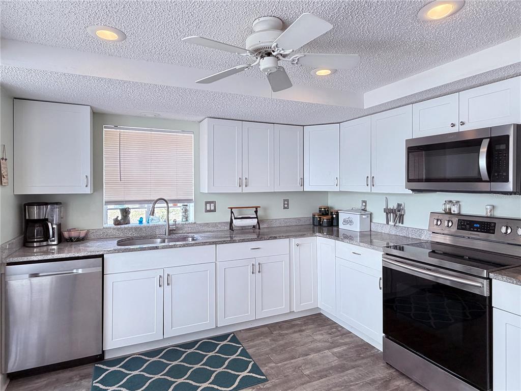 A kitchen features white cabinets, stainless steel appliances, granite countertops, and a ceiling fan — 12901 CLUB DRIVE, HUDSON, FL