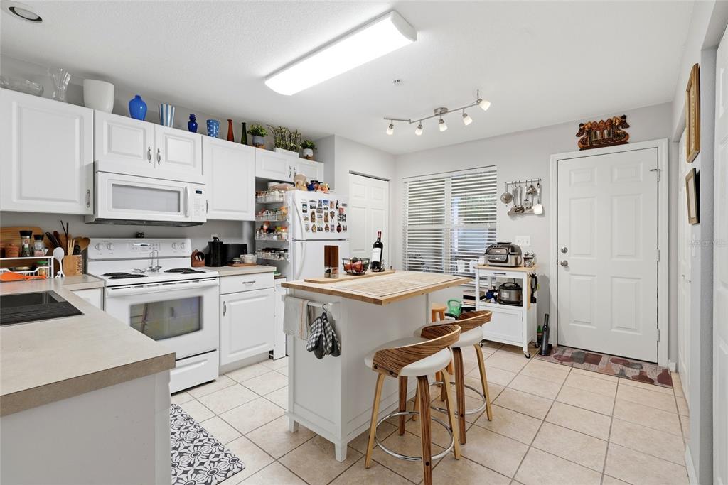 A kitchen features white cabinetry, a central island with two stools, and tile flooring — 4611 SW 48TH WAY UNIT 108, GAINESVILLE, FL