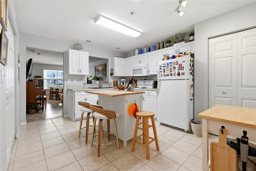 A kitchen features white cabinets, a central island with bar stools, and tile flooring — 4611 SW 48TH WAY UNIT 108, GAINESVILLE, FL