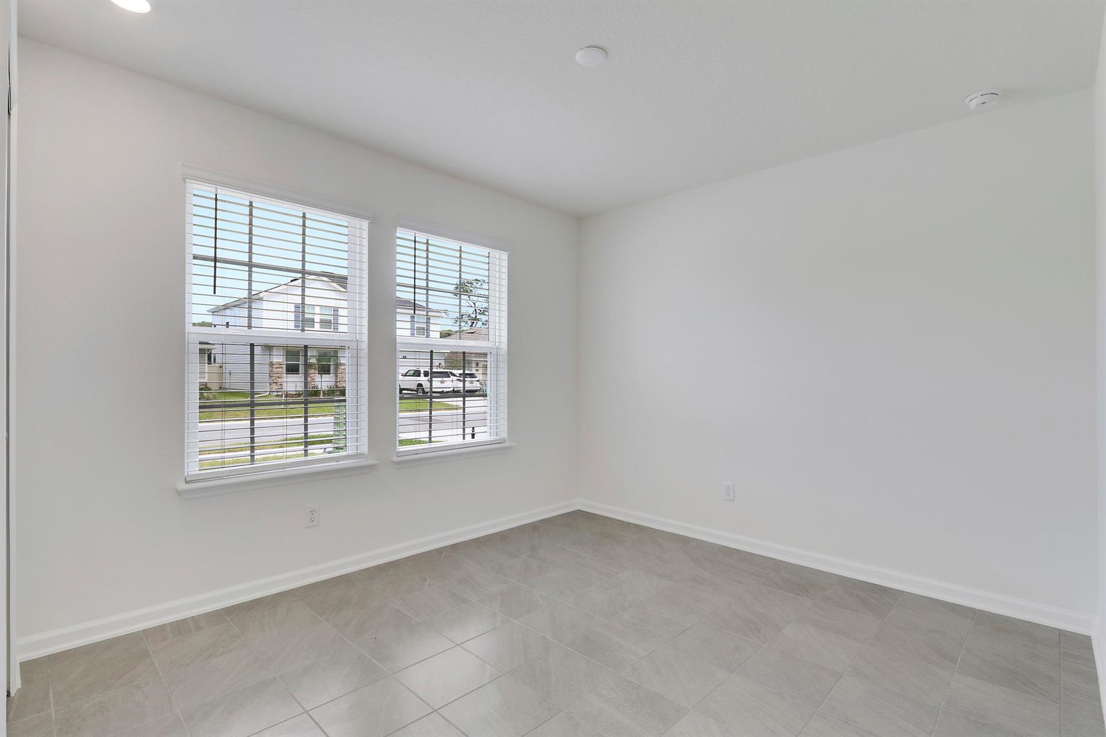 An empty room with white walls, gray tile flooring, and two windows facing a street — 65 Signet Circle, FL 32136, FL