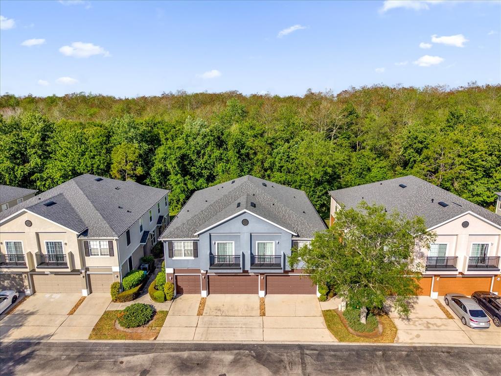An aerial view of three multi-story townhomes with attached garages and a wooded background — 6452 S GOLDENROD ROAD UNIT 26C, ORLANDO, FL