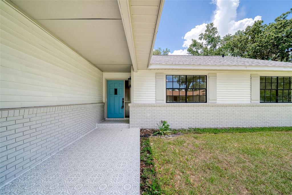 A front porch with a patterned floor leads to a bright blue door on a house — 8050 NW 48TH LANE, OCALA, FL