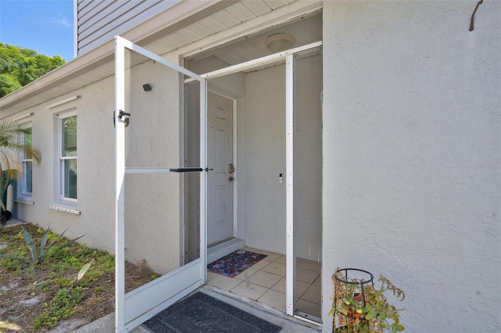 A white screen door opens to a tiled entryway with a light-colored front door — 3039 DUNHILL DRIVE, COCOA, FL
