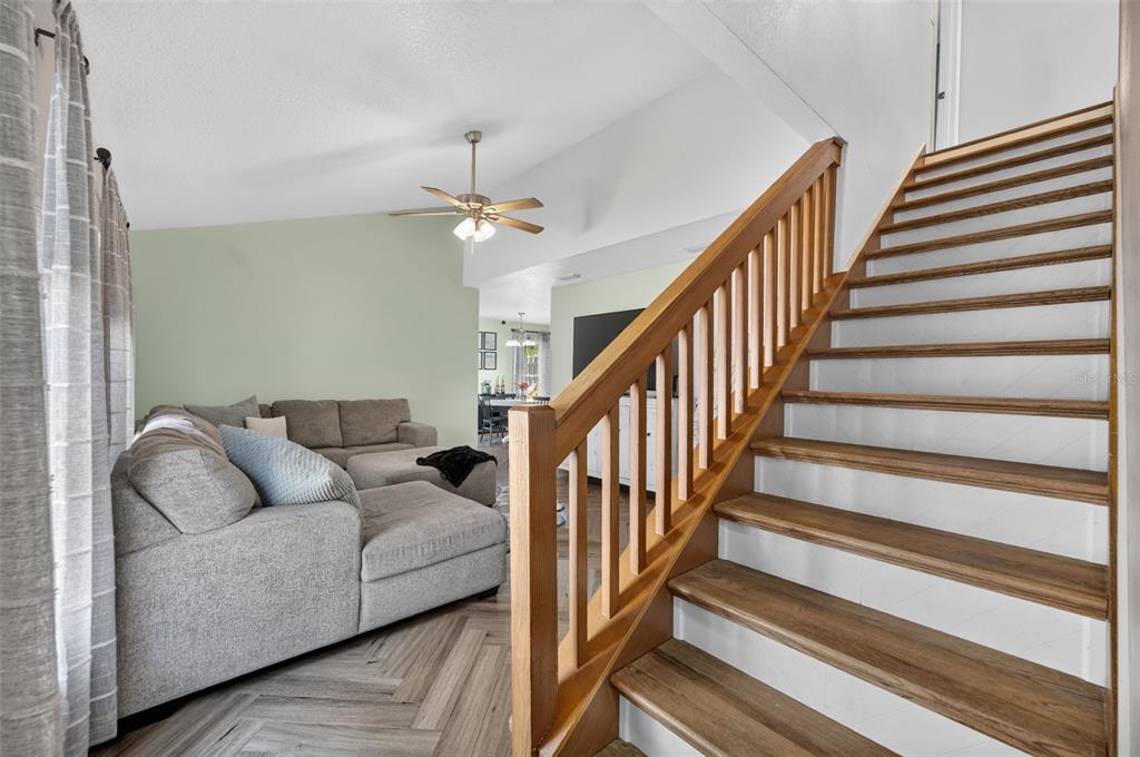 A living room with a gray sectional sofa and a wooden staircase with white risers — 3039 DUNHILL DRIVE, COCOA, FL