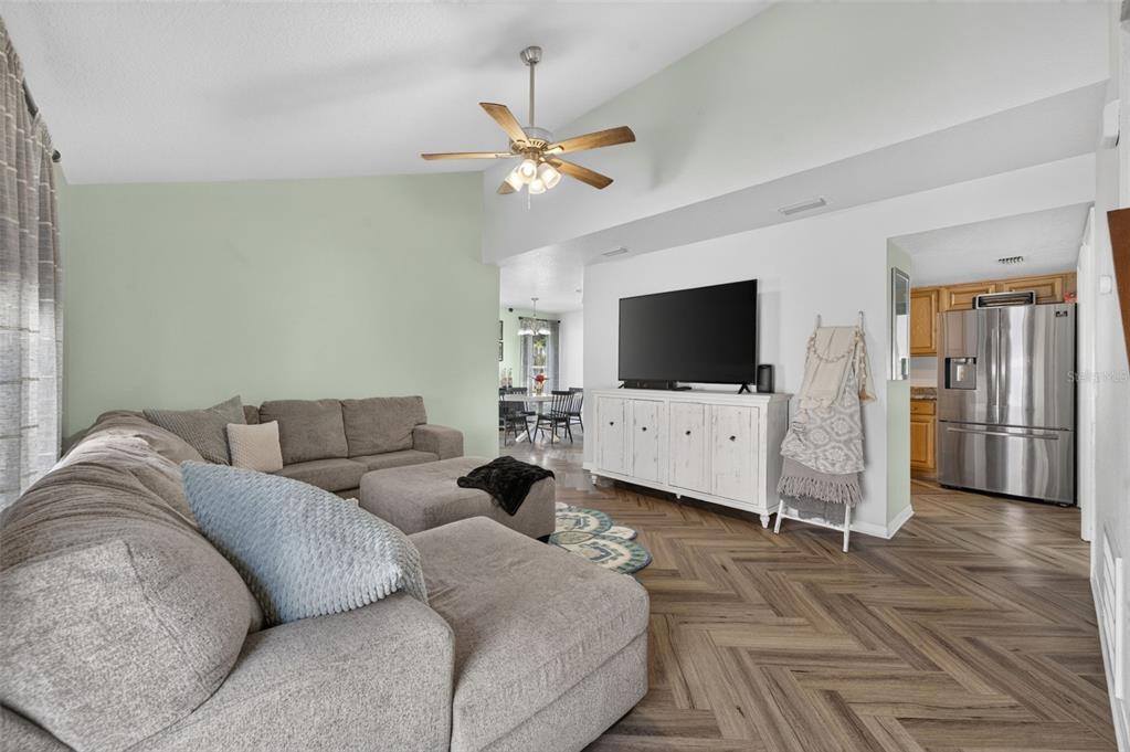 A living room features a grey sectional sofa, a white media console, and herringbone flooring — 3039 DUNHILL DRIVE, COCOA, FL