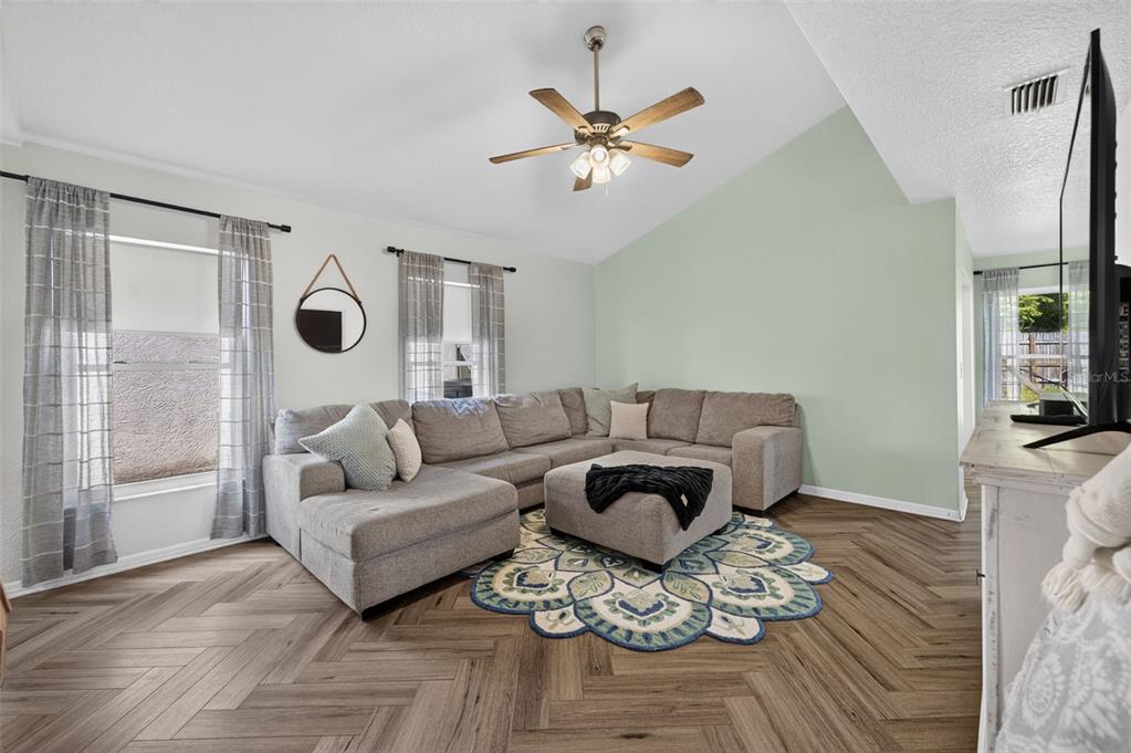 A living room features a grey sectional sofa, a patterned rug, and herringbone wood flooring — 3039 DUNHILL DRIVE, COCOA, FL