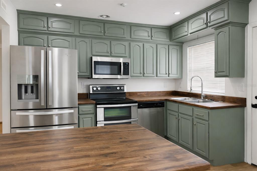 A kitchen features sage green cabinets, stainless steel appliances, and dark wood countertops — 630 TAM O SHANTER DRIVE, ORLANDO, FL