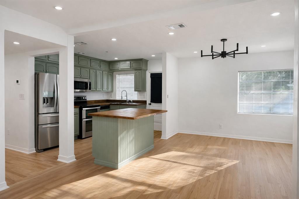 A kitchen with sage green cabinets and a wood-topped island opens to a dining area — 630 TAM O SHANTER DRIVE, ORLANDO, FL