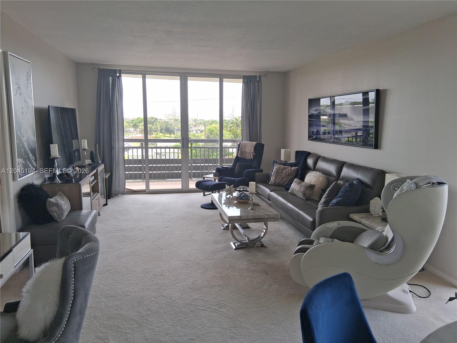 A living room features a grey sofa, a massage chair, a coffee table, and balcony access — 555 NW 4th Ave # 4250, Boca Raton FL 33432, BOCA RATON, FL
