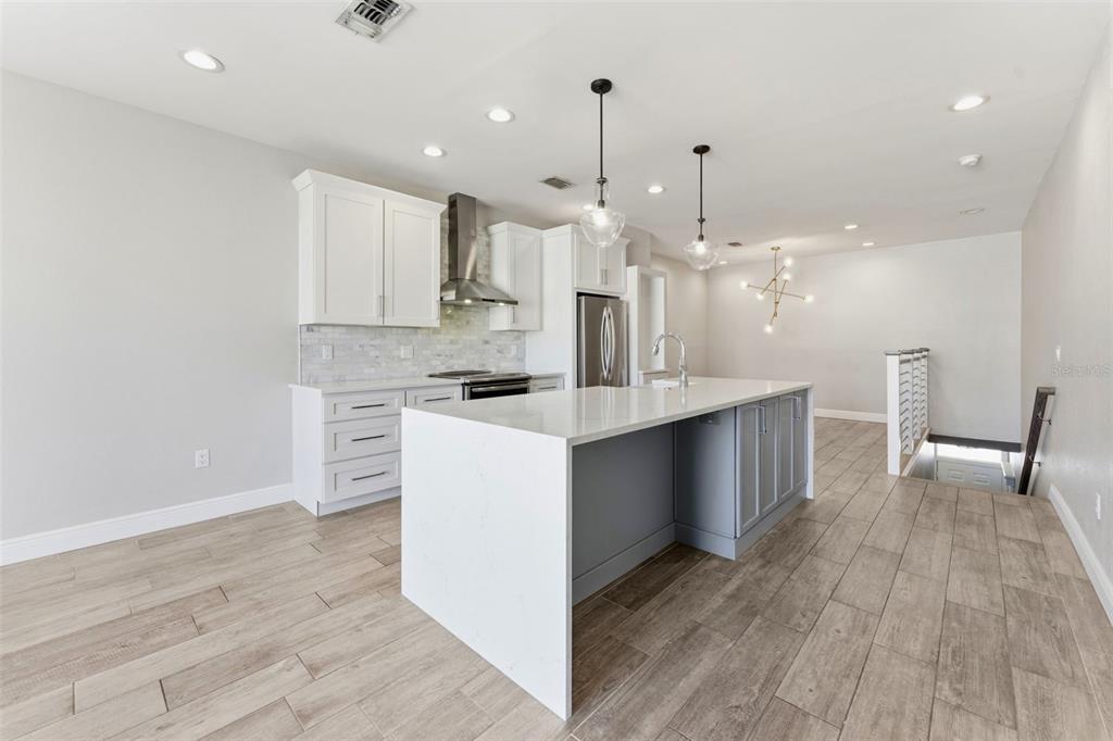 A modern kitchen features white cabinets, a gray island with a quartz countertop, and wood-look flooring — 1022 NORMANDY TRACE ROAD, TAMPA, FL