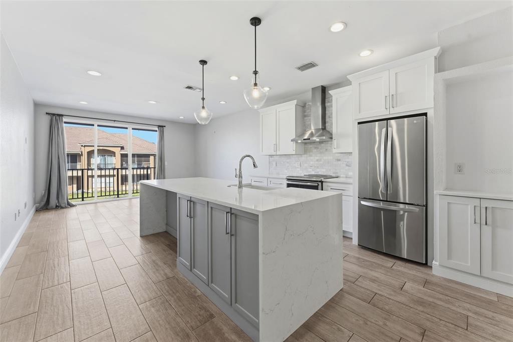 A modern kitchen features a gray island, white cabinetry, stainless steel appliances, and wood-look tile — 1022 NORMANDY TRACE ROAD, TAMPA, FL