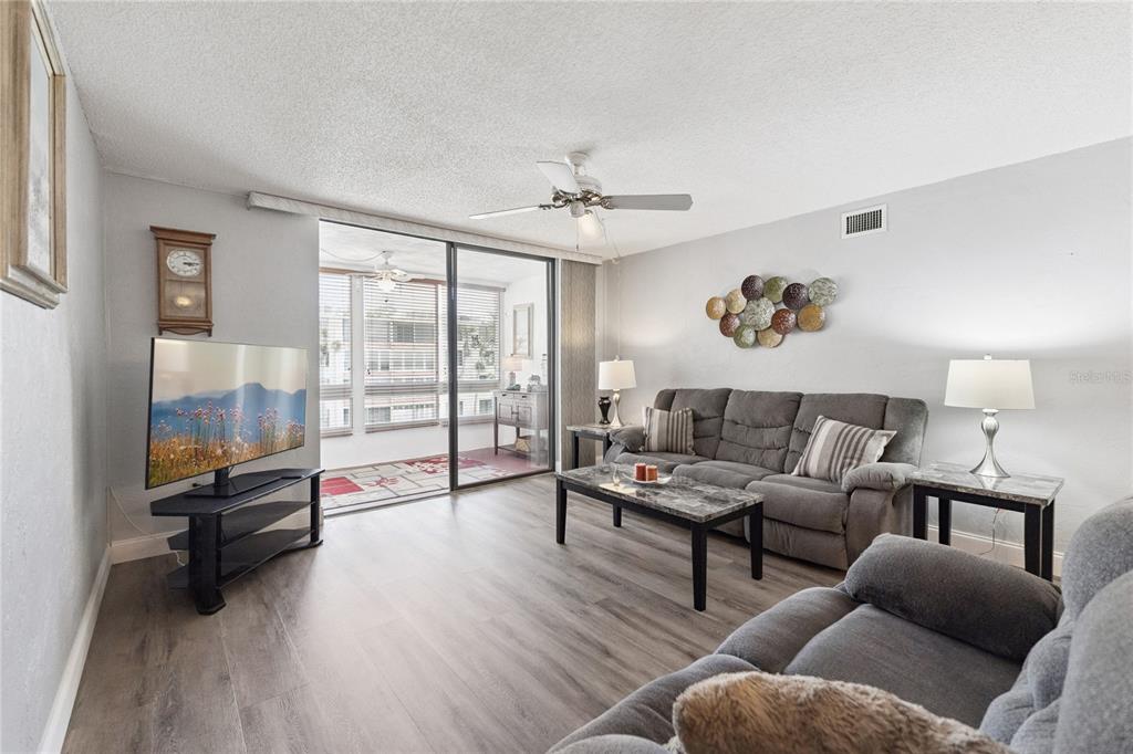 A living room features gray wood-look flooring, a gray sofa, and a sliding glass door — 325 WILDER BOULEVARD UNIT A404, DAYTONA BEACH, FL