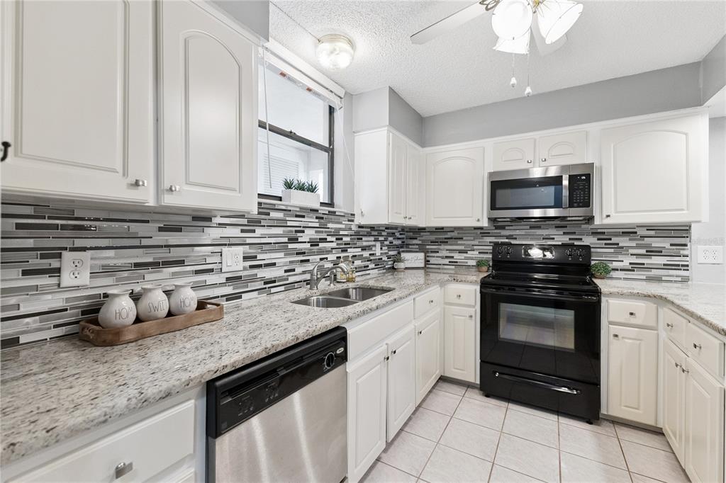 A kitchen features white cabinets, granite countertops, a stainless steel dishwasher, and a tiled backsplash — 325 WILDER BOULEVARD UNIT A404, DAYTONA BEACH, FL