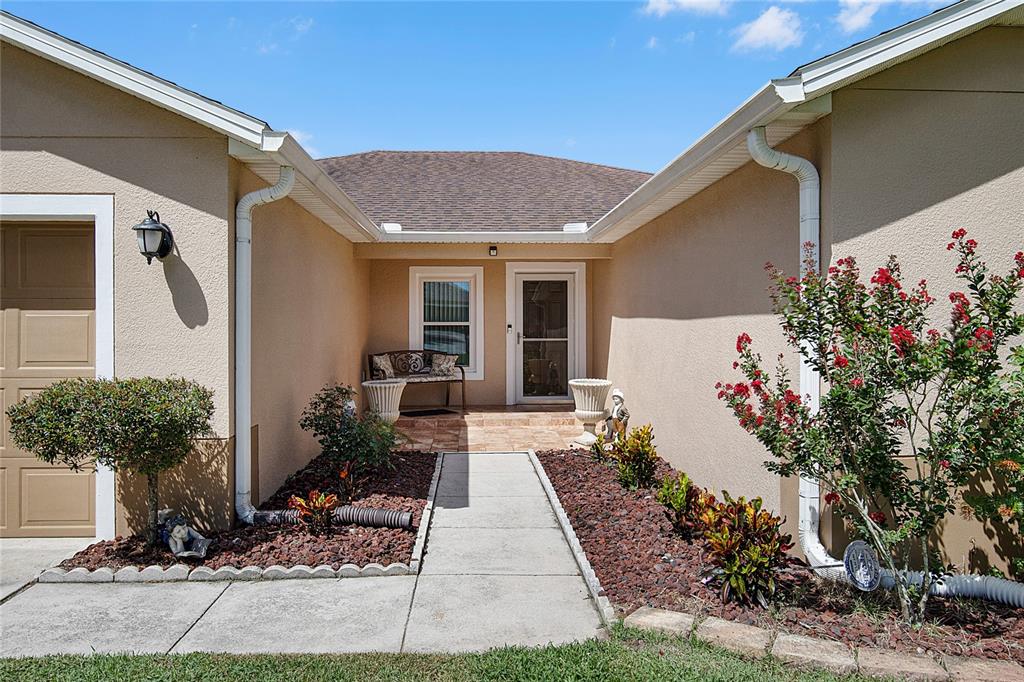 A concrete walkway leads to the front entrance of a beige house with landscaping — 2388 YELLOW GRASS COURT, APOPKA, FL