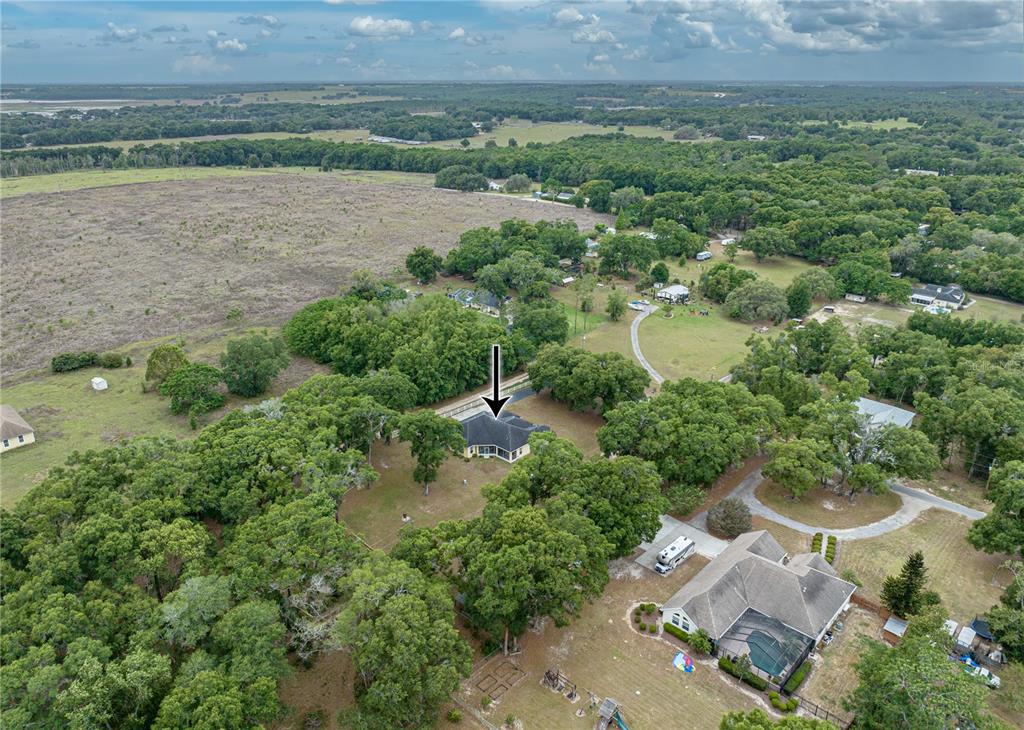An aerial view shows a house with a dark roof surrounded by trees and fields — 12806 JUDY STREET, DADE CITY, FL
