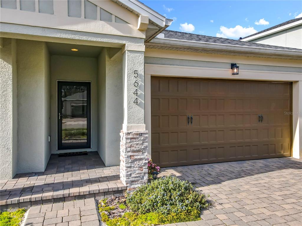 The exterior of a house features a brown garage door, a stone-accented pillar, and a paver driveway — 5644 ESTERO LOOP, PORT ORANGE, FL