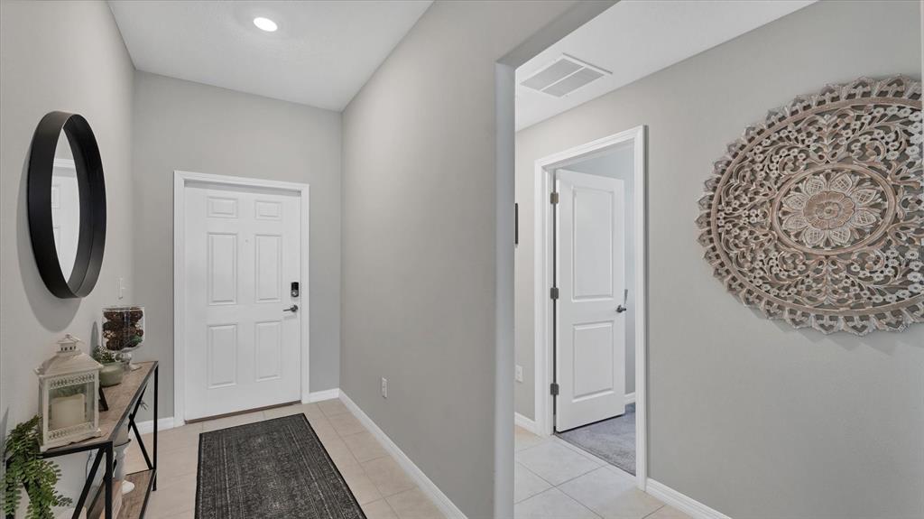 A bright entryway features light gray walls, tile flooring, a white door, and wall decor — 15423 MILLER CREEK DRIVE, RUSKIN, FL