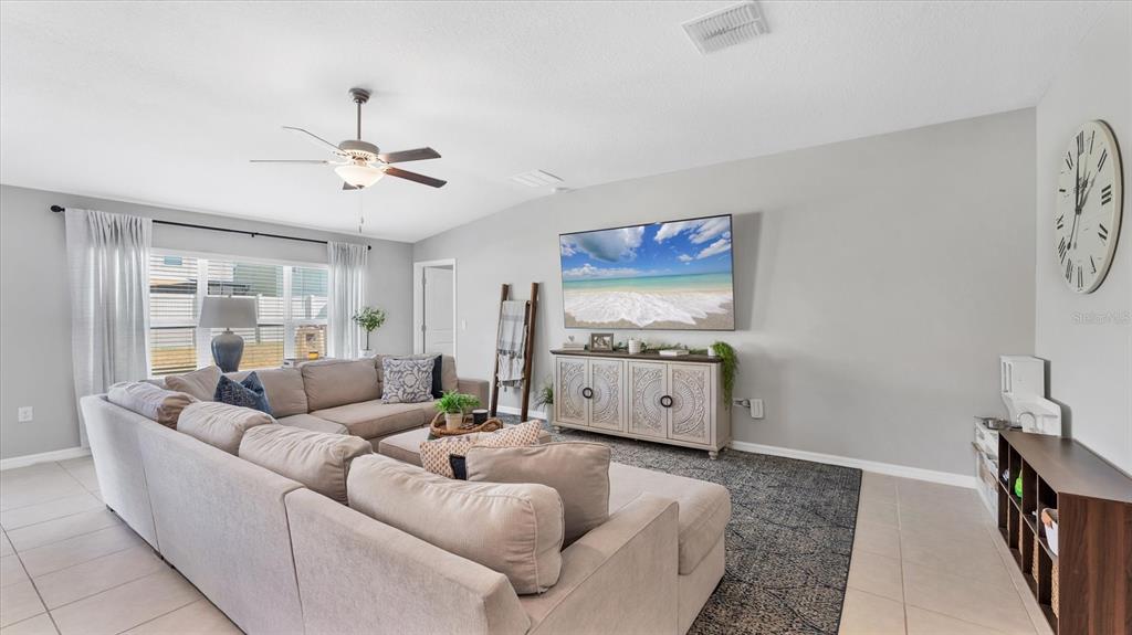 A living room features a large sectional sofa, a wall-mounted television, and a decorative clock — 15423 MILLER CREEK DRIVE, RUSKIN, FL