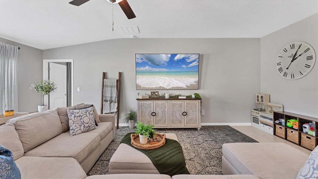 A living room features a sectional sofa, a television, a media console, and a wall clock — 15423 MILLER CREEK DRIVE, RUSKIN, FL