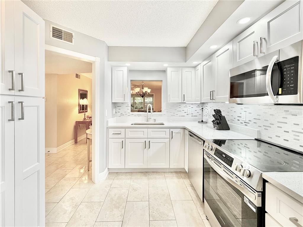 A bright kitchen features white cabinets, stainless steel appliances, and light-colored tile flooring — 1247 S MARTIN LUTHER KING JUNIOR AVENUE UNIT D103, CLEARWATER, FL