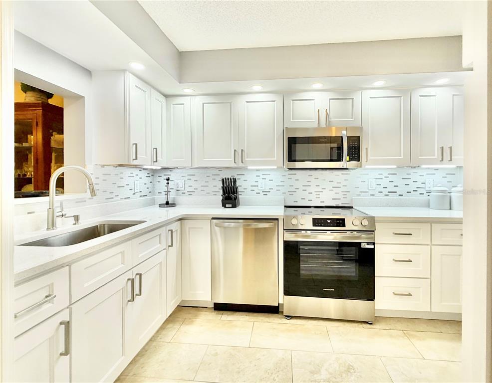 A modern kitchen featuring white cabinets, stainless steel appliances, and a light-colored tile backsplash — 1247 S MARTIN LUTHER KING JUNIOR AVENUE UNIT D103, CLEARWATER, FL