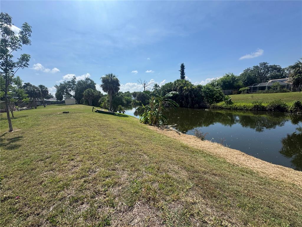 A grassy backyard slopes down toward a small pond with trees and nearby houses — 21239 COTTONWOOD AVENUE, PORT CHARLOTTE, FL