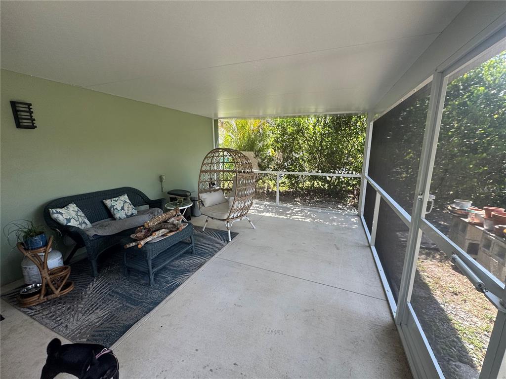 A screened-in patio features a wicker sofa, a hanging chair, and a concrete floor — 21239 COTTONWOOD AVENUE, PORT CHARLOTTE, FL