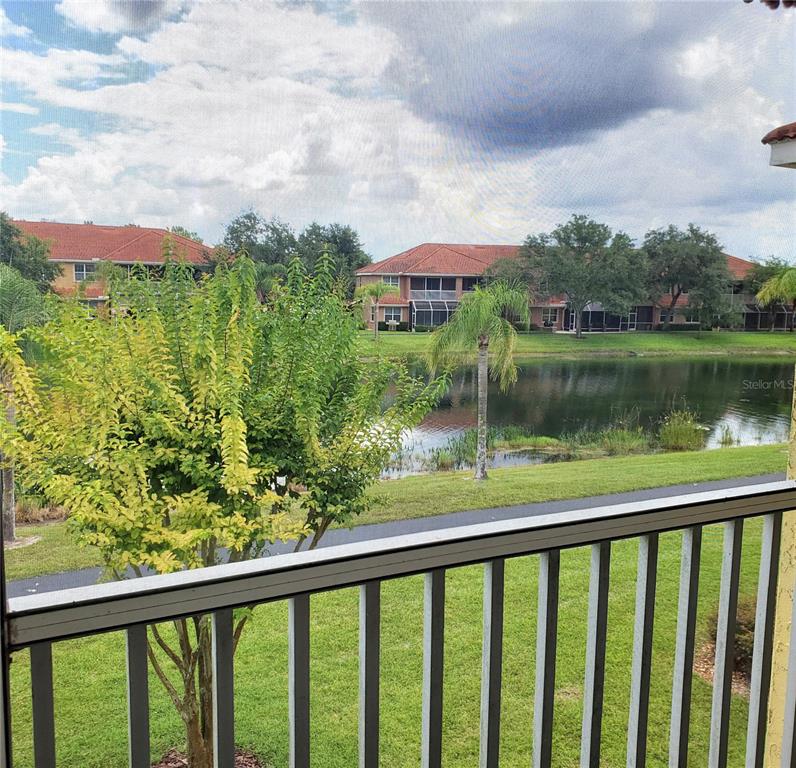 A view from a screened balcony overlooking a pond, green lawn, and residential buildings — 6750 DALI AVENUE UNIT 206, LAND O LAKES, FL