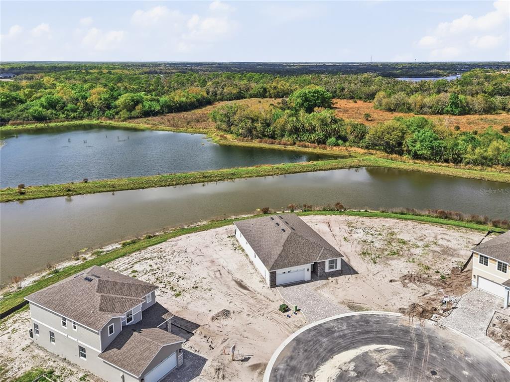 An aerial view shows three new houses under construction near a pond and wooded area — 14511 BANKS COURT, PARRISH, FL