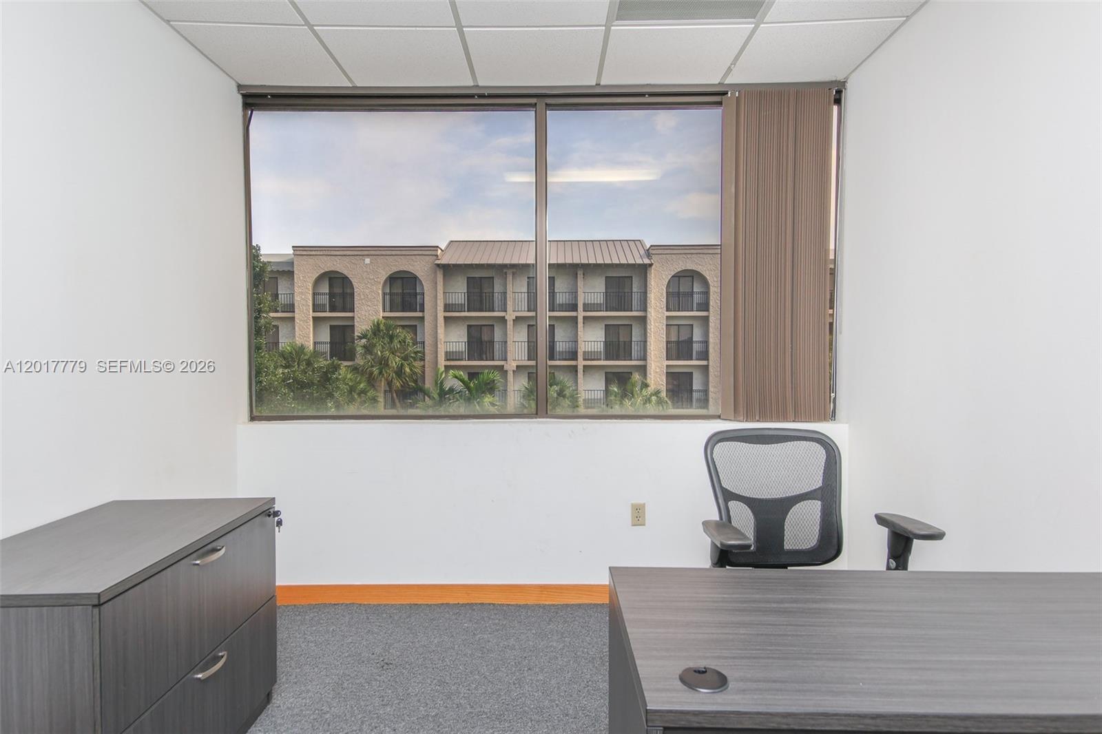 An office space features a desk, a chair, gray carpeting, and a large window view — 1900 Glades Rd # 276, Boca Raton FL 33431, BOCA RATON, FL