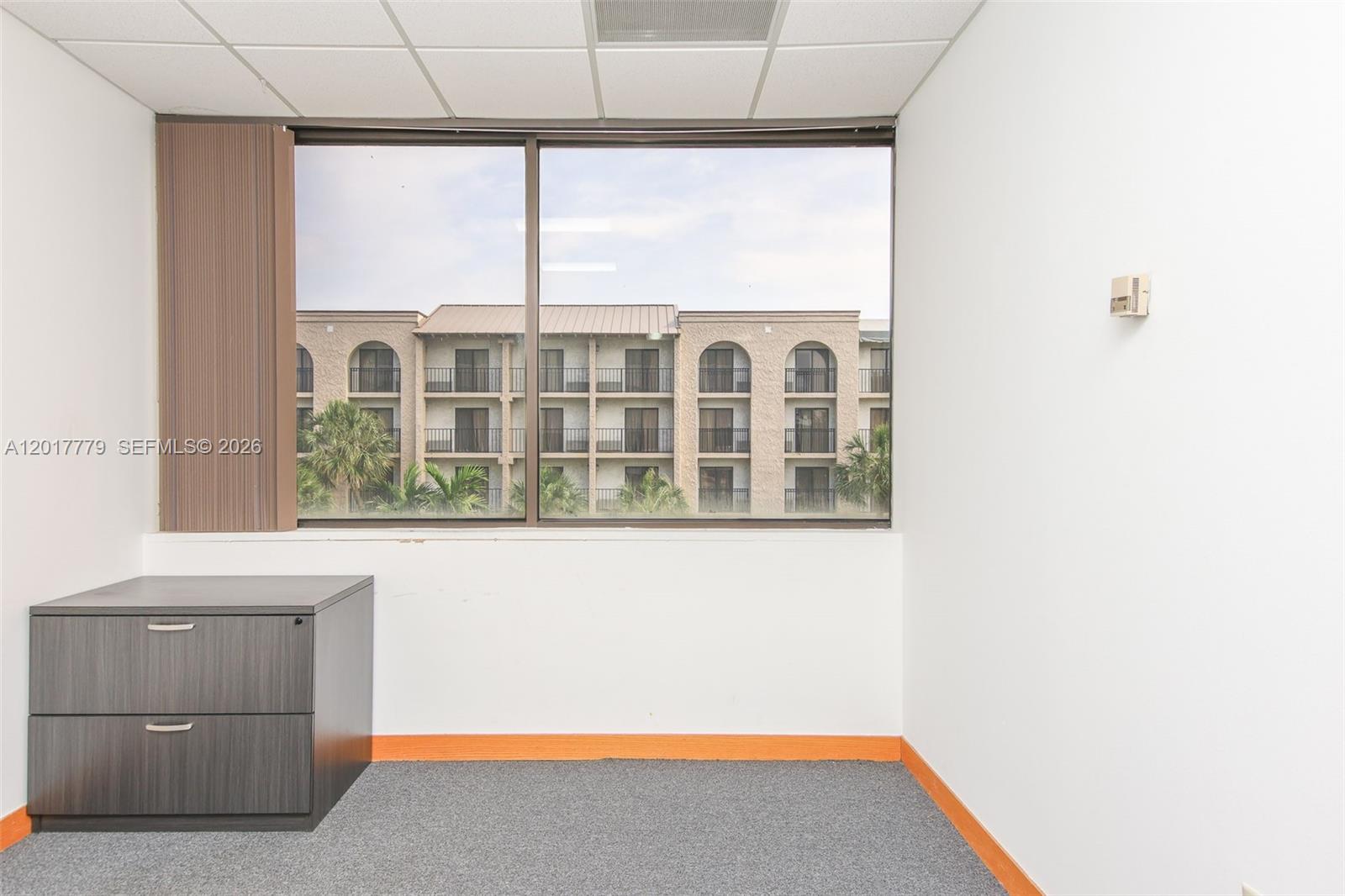 An office space features gray carpet, a dark wood filing cabinet, and a large window — 1900 Glades Rd # 276, Boca Raton FL 33431, BOCA RATON, FL