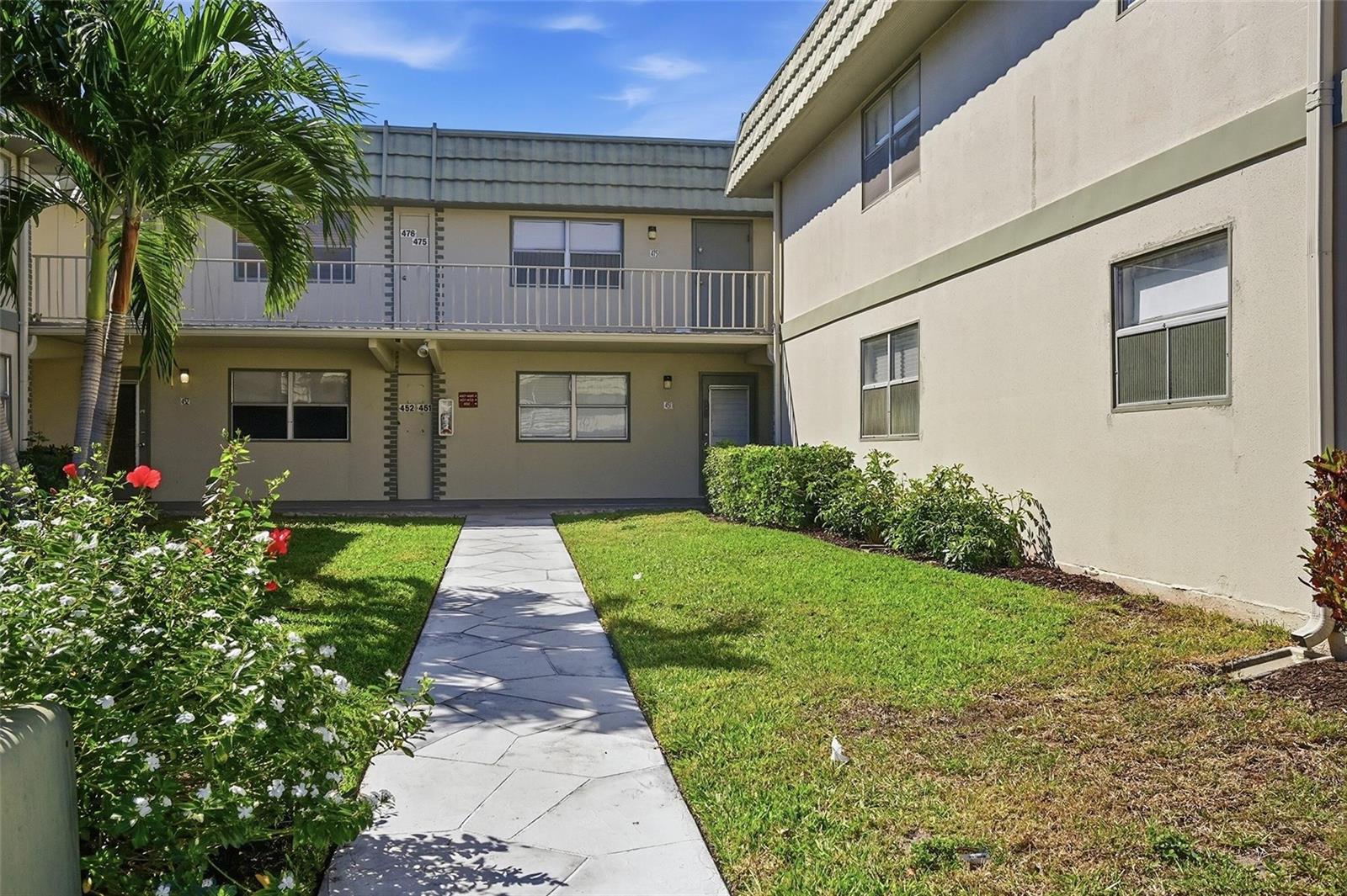 A two-story apartment building exterior features a concrete walkway leading to a central entrance — 451 Monaco J # j, Delray Beach FL 33446, DELRAY BEACH, FL