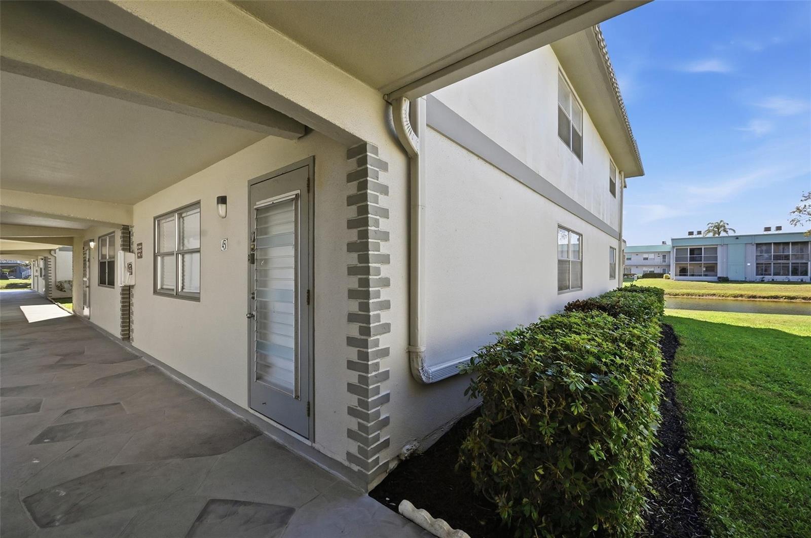 An exterior view of a ground-level apartment entrance with a covered walkway and adjacent landscaping — 451 Monaco J # j, Delray Beach FL 33446, DELRAY BEACH, FL