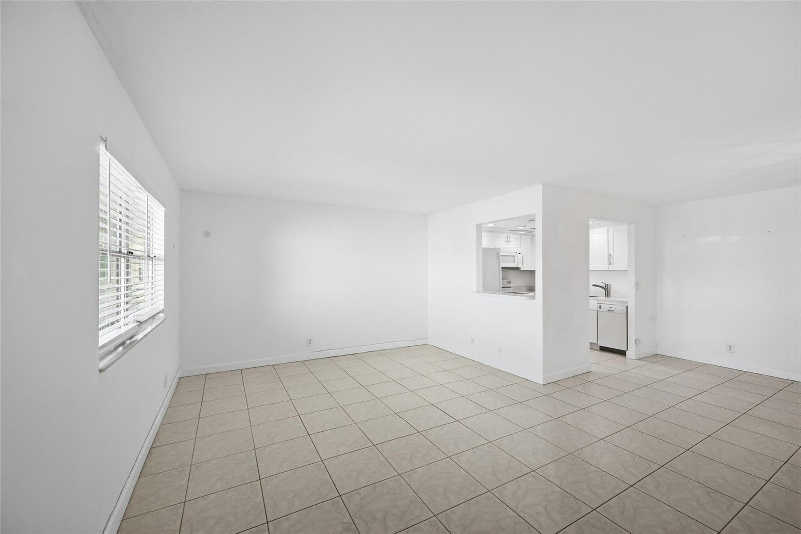 An empty room with white walls, beige tile flooring, and a pass-through to the kitchen — 451 Monaco J # j, Delray Beach FL 33446, DELRAY BEACH, FL