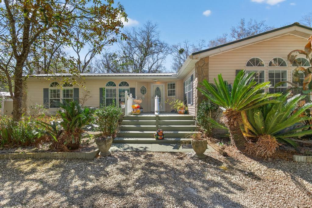 A single-story house with light siding, a front porch, and gravel driveway under trees — 8321 HARDWOOD LANDING ROAD, ST AUGUSTINE, FL