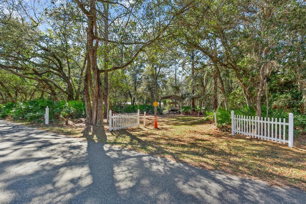 A gravel driveway leads through a white picket fence into a wooded lot with trees — 8321 HARDWOOD LANDING ROAD, ST AUGUSTINE, FL