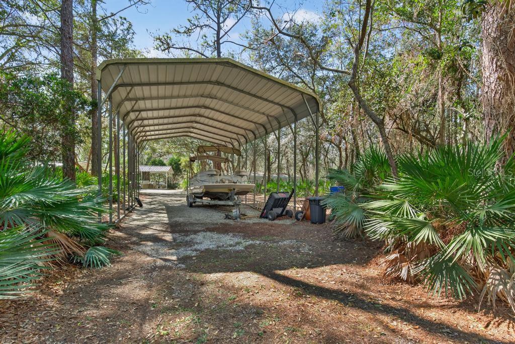 A pontoon boat is parked under a metal carport in a wooded outdoor area — 8321 HARDWOOD LANDING ROAD, ST AUGUSTINE, FL