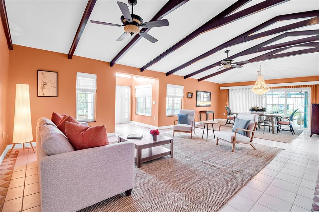 A living room with vaulted ceilings, exposed beams, orange walls, and a large area rug — 608 GARDENIA DRIVE, VENICE, FL