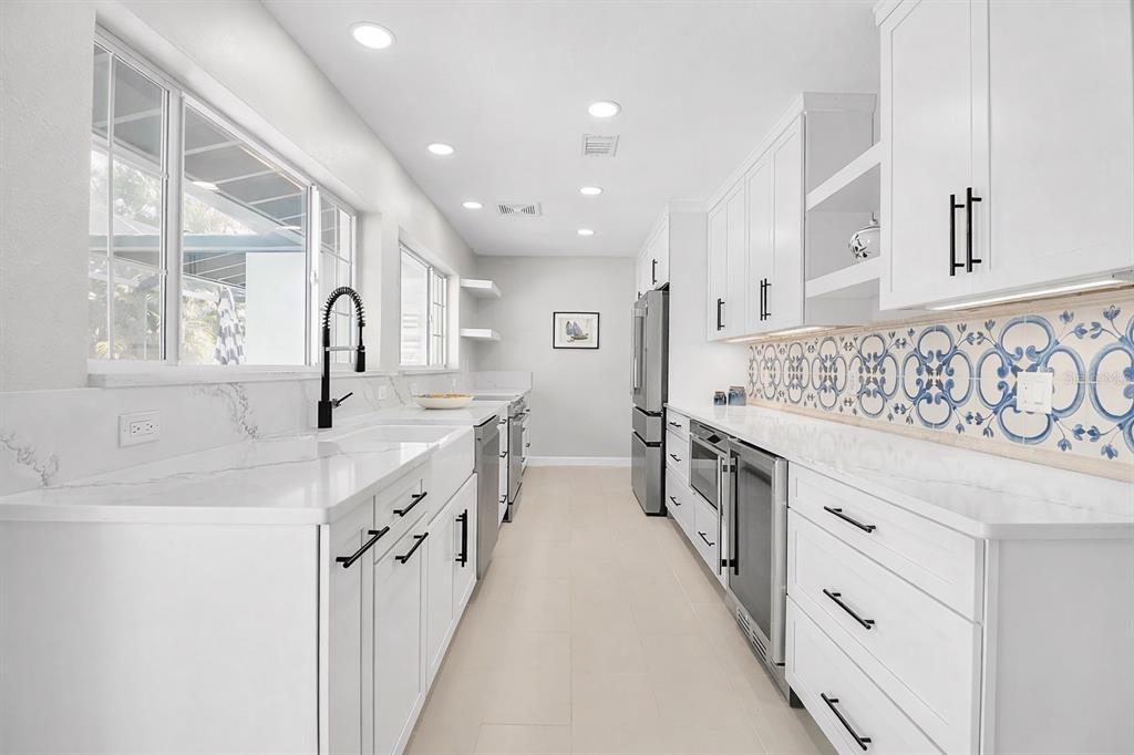 A bright galley kitchen features white cabinets, quartz countertops, and a decorative blue-patterned tile backsplash — 608 GARDENIA DRIVE, VENICE, FL
