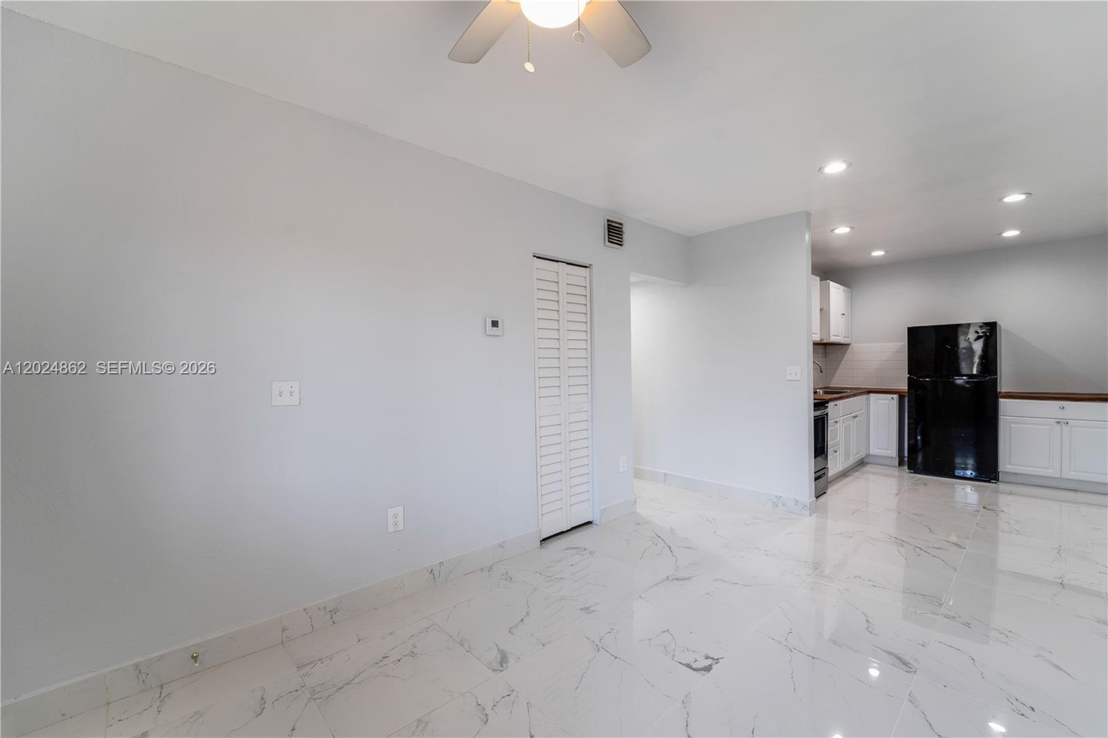 A room with white marble-patterned tile flooring leads into a kitchen with white cabinets — 22300 SW 117th Ave # 4, Miami FL 33170, MIAMI, FL