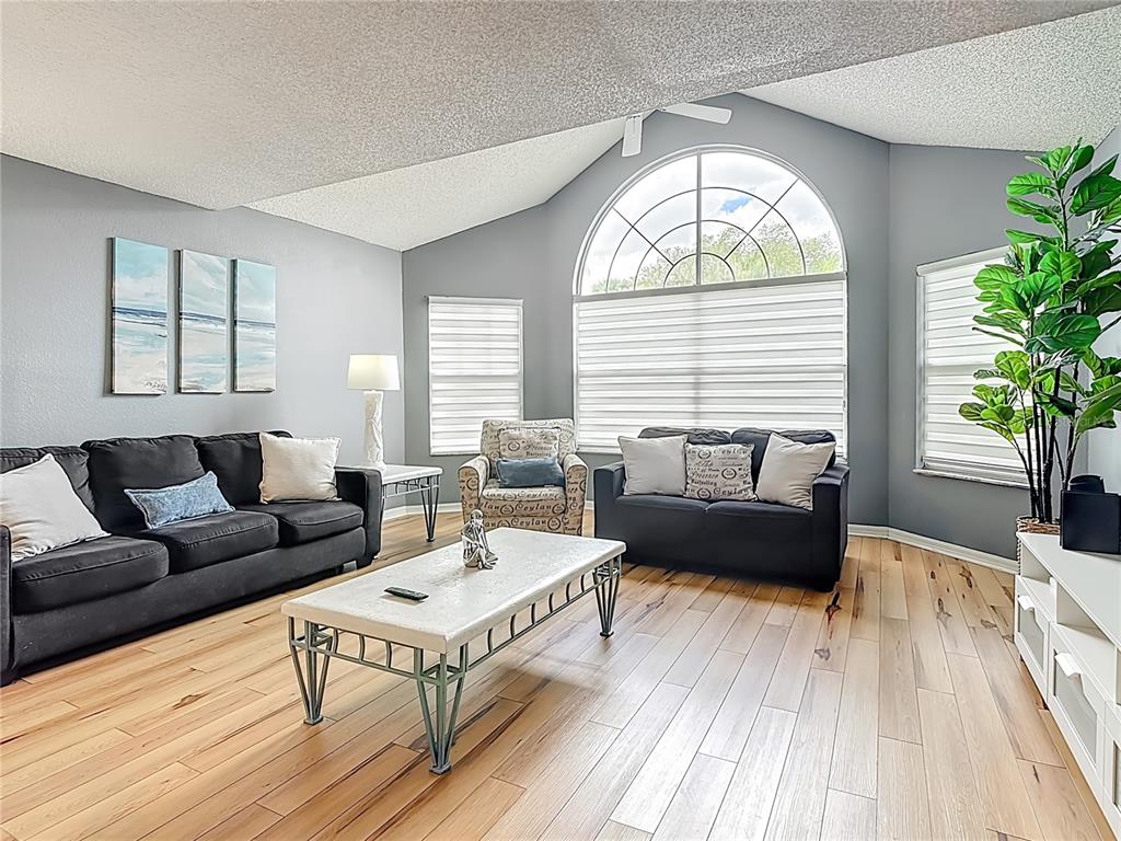 A living room features a vaulted ceiling, light wood flooring, dark sofas, and a large window — 2753 N POINCIANA BOULEVARD UNIT 37, KISSIMMEE, FL