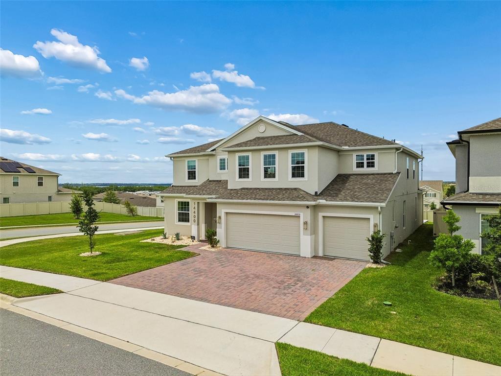A two-story suburban house with a brick driveway, three-car garage, and light-colored siding — 14400 NOTO AVENUE, CLERMONT, FL