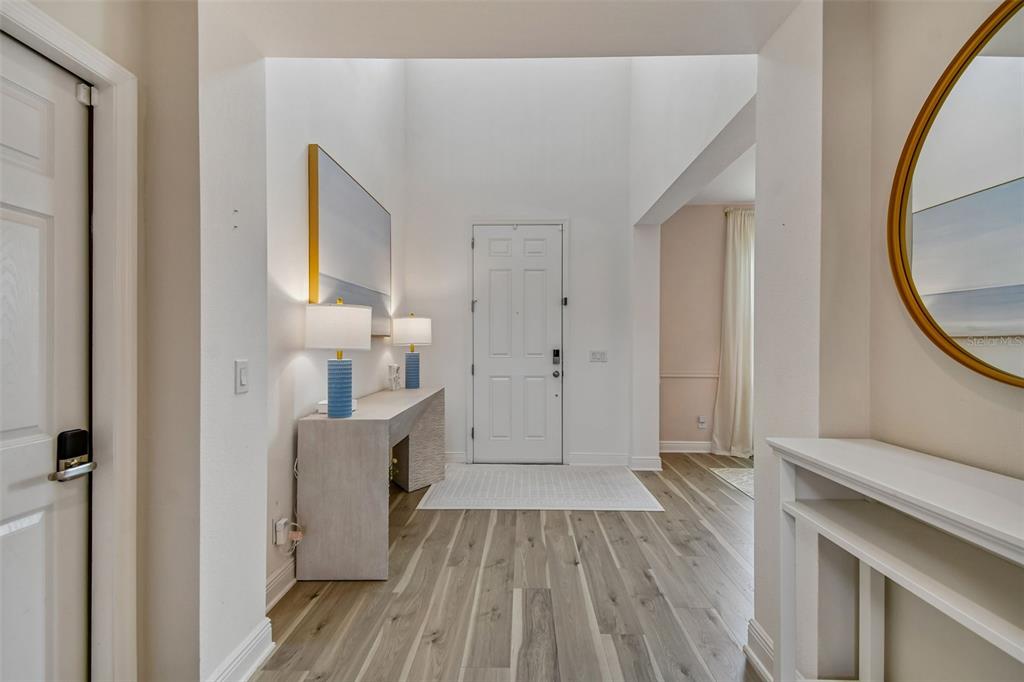 A bright entryway features light wood flooring, a console table with lamps, and a white door — 14400 NOTO AVENUE, CLERMONT, FL