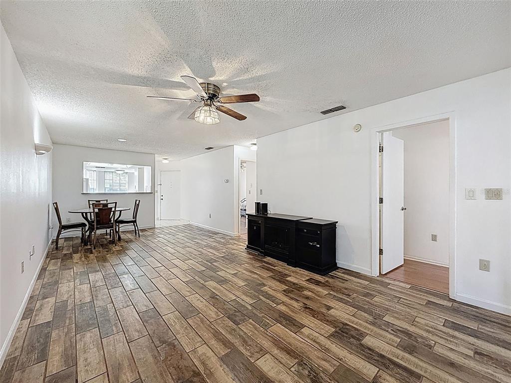 A living and dining area features wood-look tile flooring, a beige sofa, and a round table — 11403 VERSAILLES LANE UNIT E, PORT RICHEY, FL