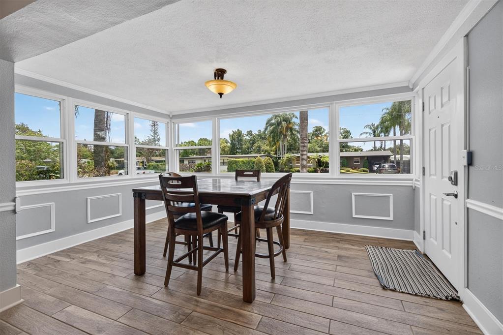 A dining area with wood-look tile floors, a wooden table, and large windows overlooking trees — 3701 VIRGINIA DRIVE, ORLANDO, FL